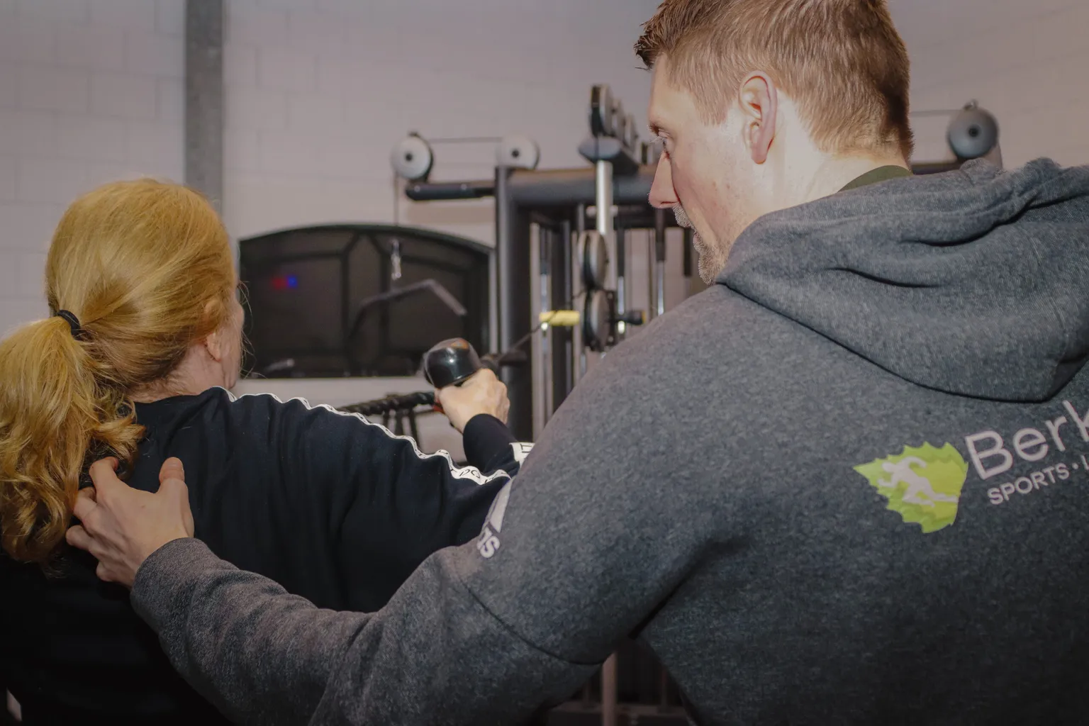 Personal trainer van BerkSports begeleidt een sporter bij een oefening aan het kabelstation