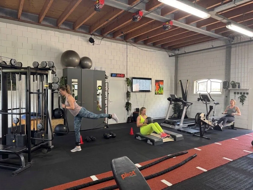 Drie sporters tijdens een BBB-training bij BerkSports in Hoofddorp: een beenoefening aan het kabelstation, buikspieroefeningen met een medicijnbal en roeien