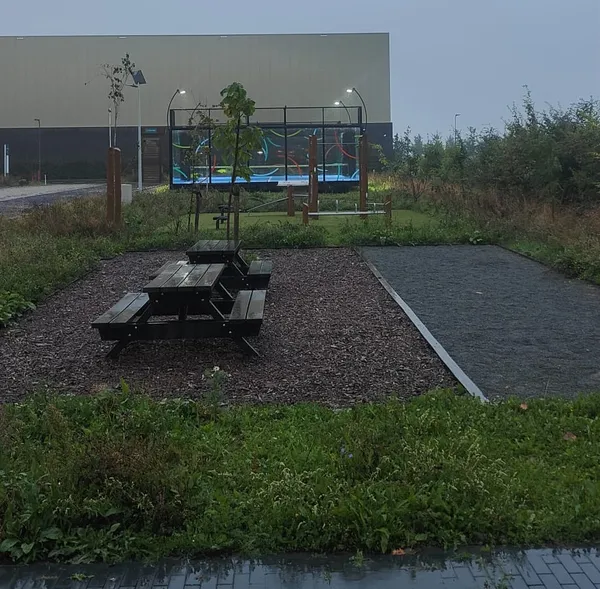 De padelbaan in de schemering, verlicht, gezien vanaf de straat met een picknicktafel op de voorgrond.