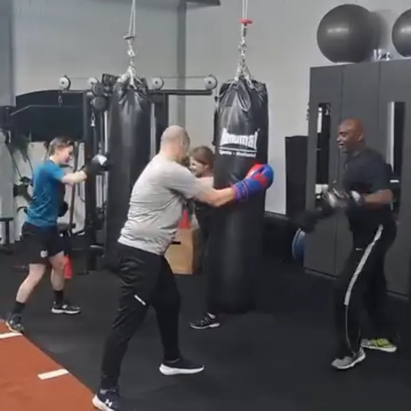 Vier deelnemers met bokshandschoenen trainen op bokszakken in de zaal van BerkSports.