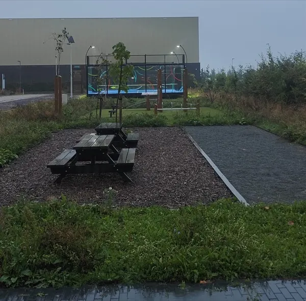 De padelbaan in de schemering, verlicht, gezien vanaf de straat met een picknicktafel op de voorgrond.