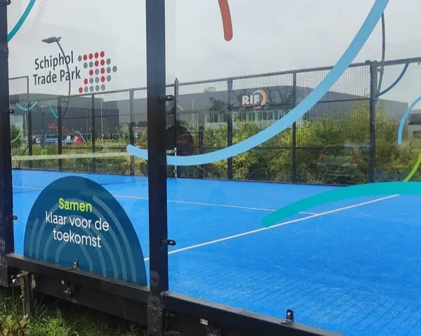 De padelbaan op Schiphol Trade Park in Hoofddorp: blauwe ondergrond, glazen wanden en een zwart hek.