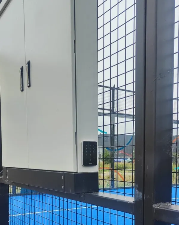 Het cijferslot naast de deur van de padelbaan, gemonteerd op een witte kast.