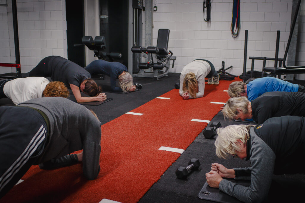 Groep sporters in plankhouding op de rode baan tijdens een groepstraining bij BerkSports