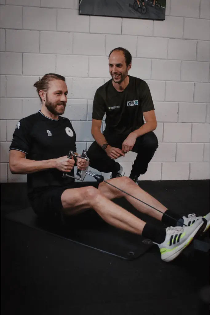 Trainer van BerkSports begeleidt een lachende sporter op de roeitrainer in Hoofddorp